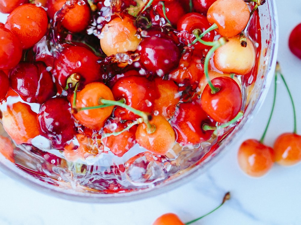 a glass bowl filled with cherries on top of a table