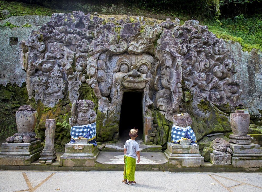 a young boy standing in front of a carved cave