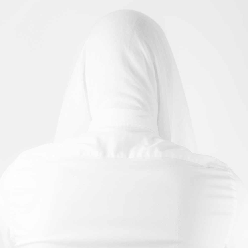 a woman in a white hoodie is standing in front of a white wall