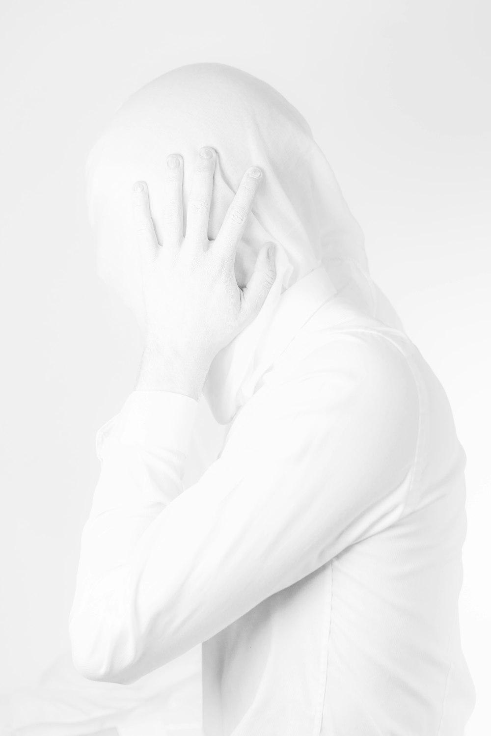 a man in a white shirt covers his face with his hands