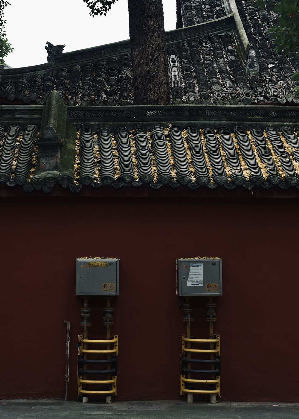 a red wall with two metal boxes next to a tree