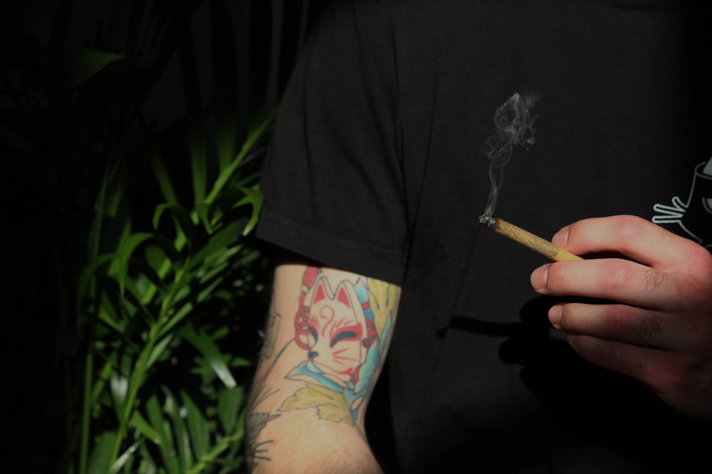 Ein Mann mit Tattoos hält eine Zigarette in der Hand