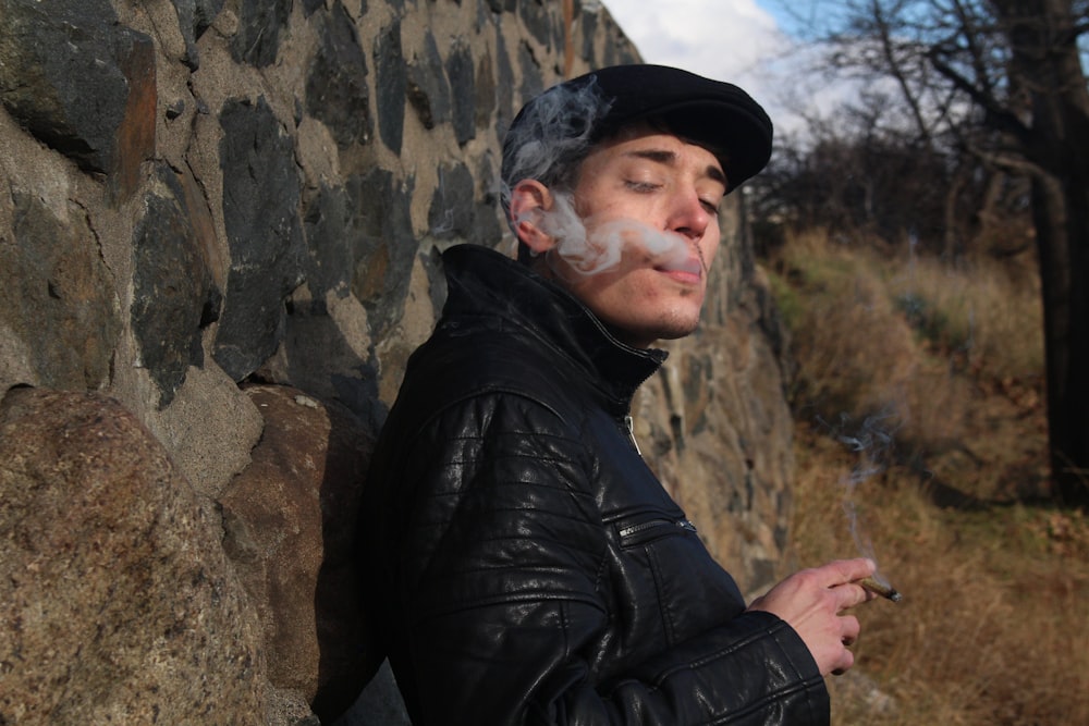 a man smoking a cigarette next to a stone wall