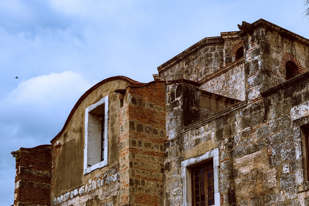 an old brick building with two windows and a bird flying in the sky