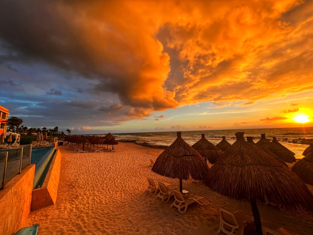 a sunset view of a beach with thatched umbrellas