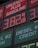 A large gas station price sign displays fuel prices with LED lights. The sign includes sections for unleaded gasoline, diesel, and other fuel types, with each section prominently showing prices in red and green LED numbers.