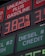 A large gas station price sign displays fuel prices with LED lights. The sign includes sections for unleaded gasoline, diesel, and other fuel types, with each section prominently showing prices in red and green LED numbers.