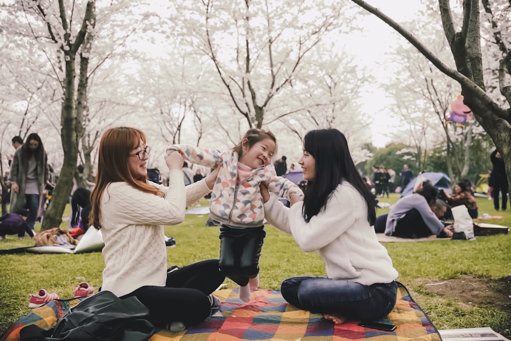 a group of women sitting on top of a blanket in a park