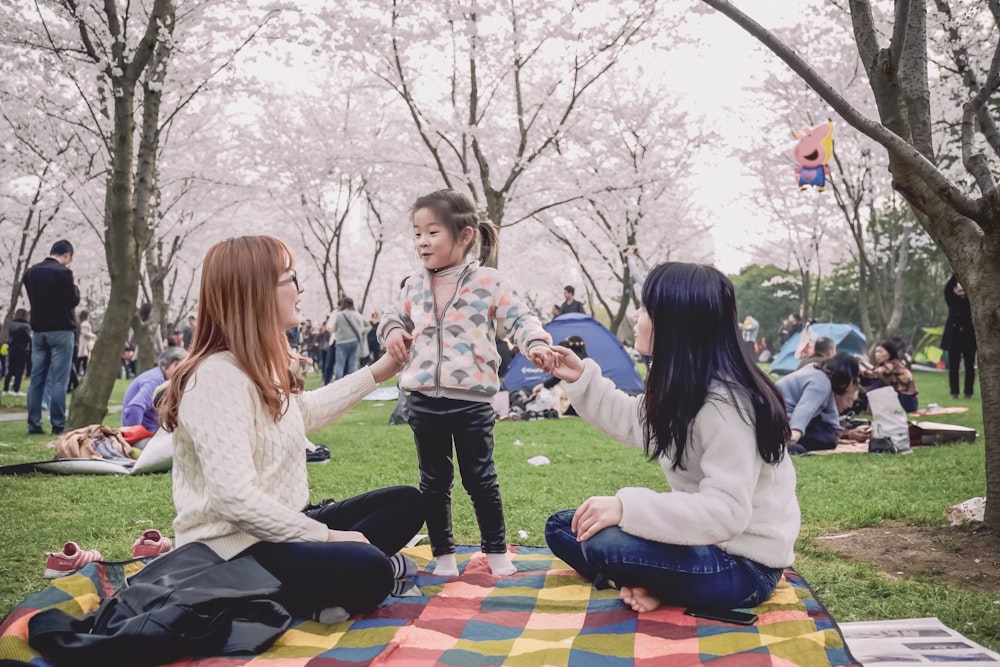 a group of women sitting on top of a blanket in a park