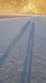 An intimate black-and-white image of a couple holding hands, their shadows stretching on soft sand.