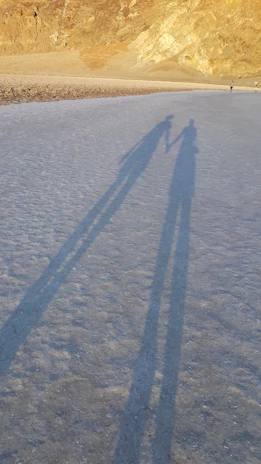 An intimate black-and-white image of a couple holding hands, their shadows stretching on soft sand.
