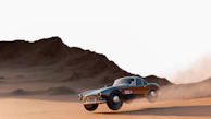 Dusty Baja desert trail with a vintage race car kicking up sand under a bright blue sky.