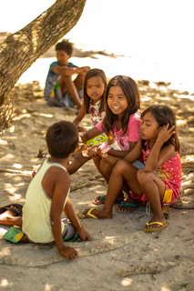 A group of kids sitting under a big tree, watching birds fly and chirp around them