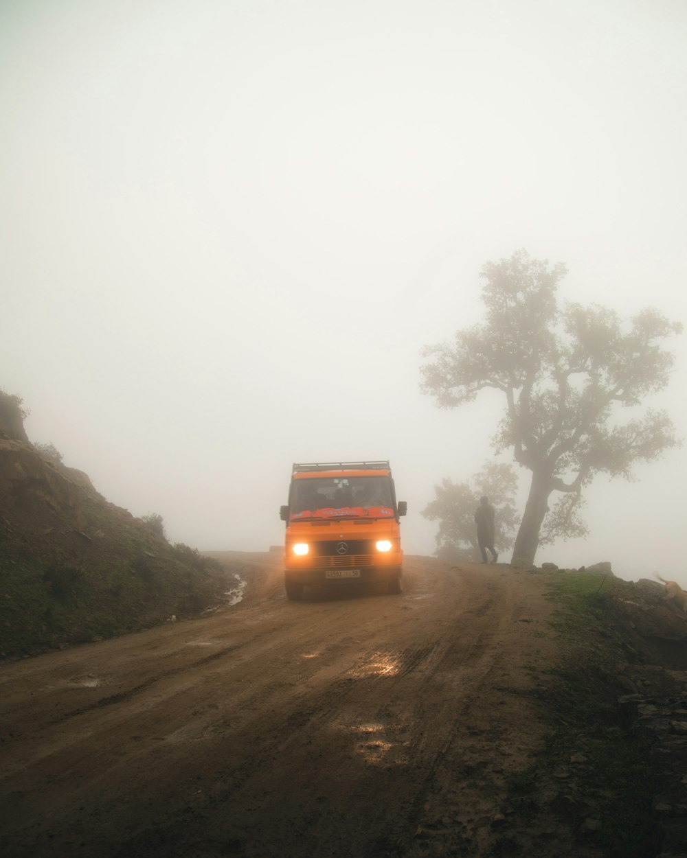 a truck driving down a dirt road in the fog
