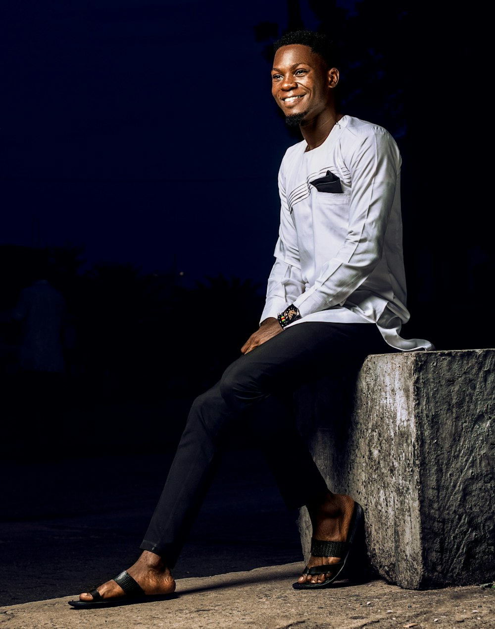 a man in a white shirt and black pants sitting on a cement block