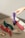 Various vibrantly colored personal massagers are arranged on a textured fabric surface. A hand with a ring is reaching towards a purple massager. The shadow and light suggest it is taken during the day.