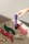 Various vibrantly colored personal massagers are arranged on a textured fabric surface. A hand with a ring is reaching towards a purple massager. The shadow and light suggest it is taken during the day.