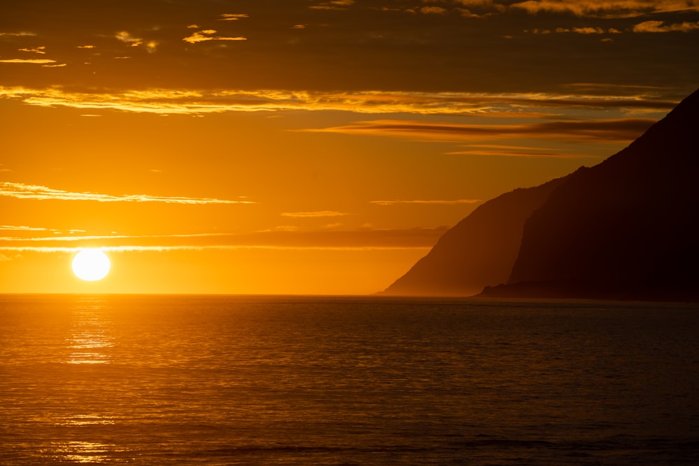 the sun is setting over the ocean with mountains in the background