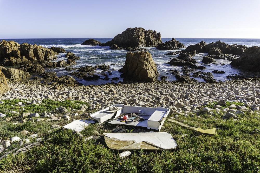 a couch sitting on top of a rocky beach next to the ocean