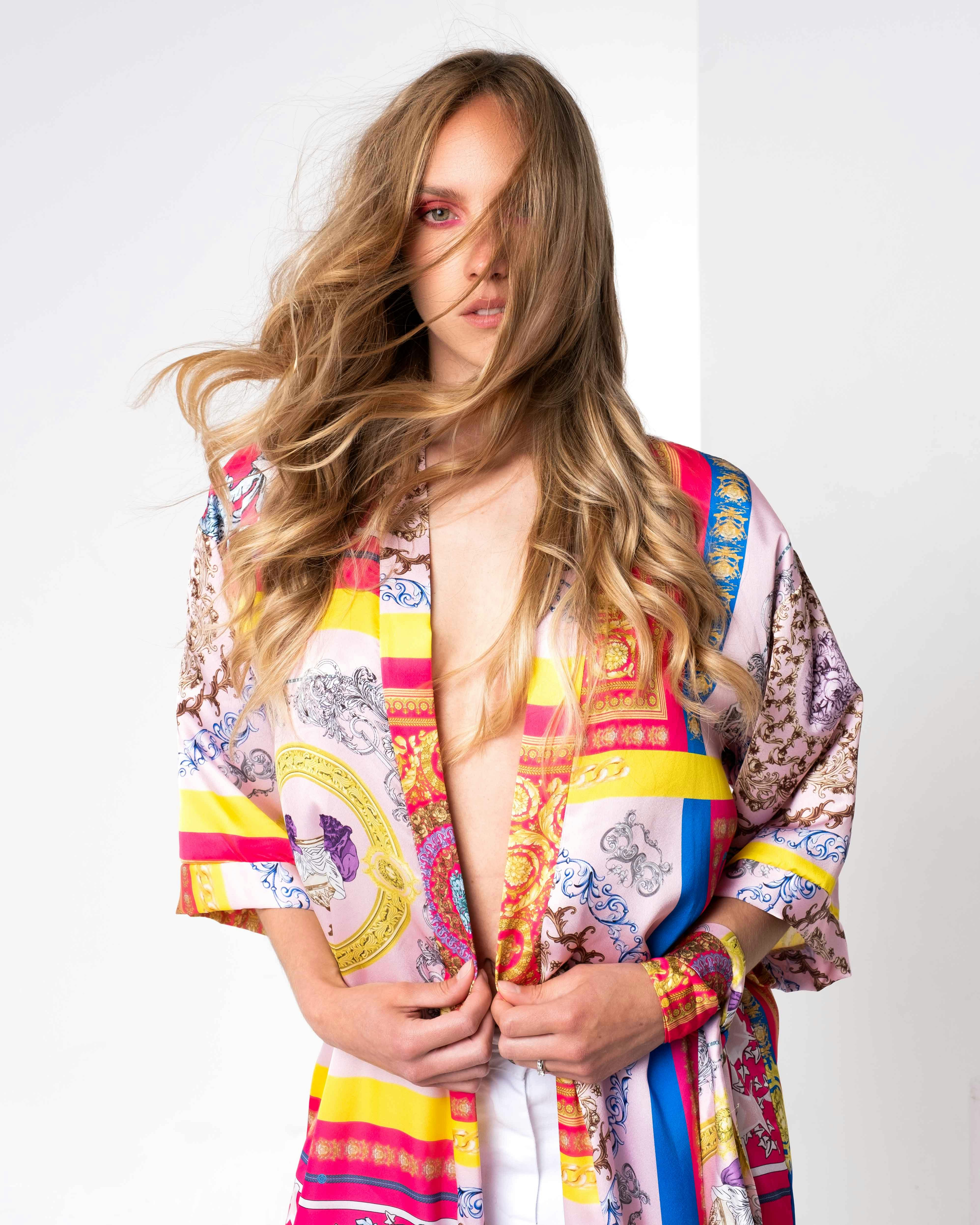Studio portrait photograph of a woman in a vibrant, patterned robe against a white studio backdrop.