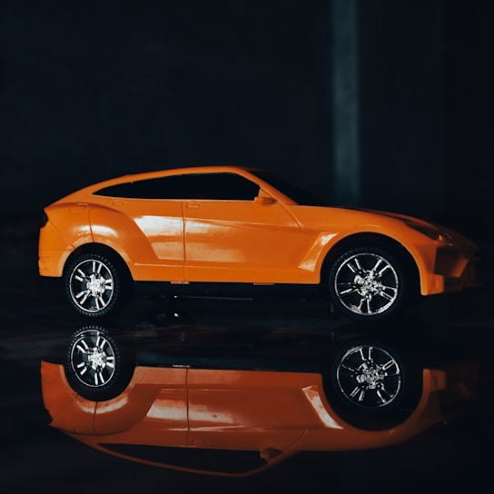 Close-up of a sleek geometric prototype model in graphite gray and signal orange accents on a light paper background