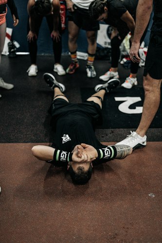 A person sitting on a gym bench holding their head, looking fatigued