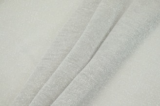 Close-up of luxury collection sheets with subtle sheen and elegant folds in light grey tones.