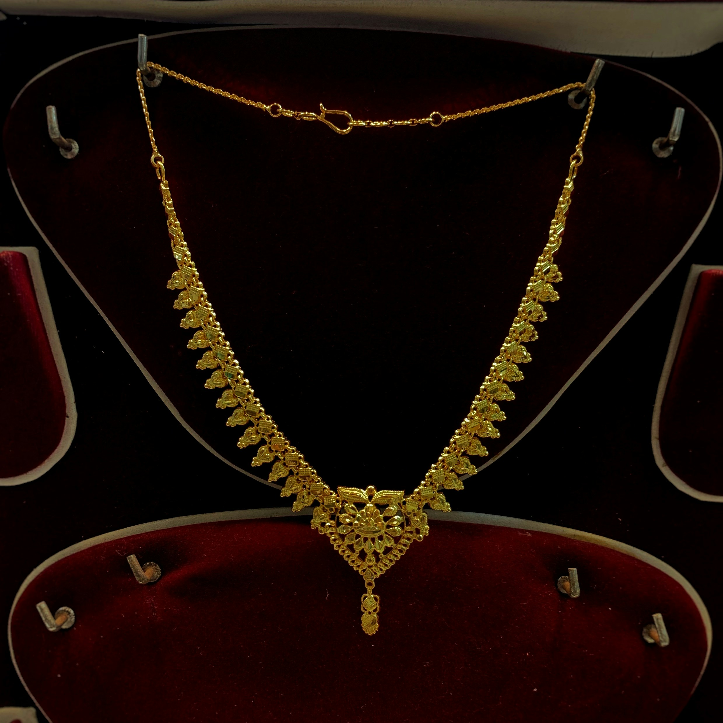 Gold necklace close-up showing intricate arabesque pattern detail on dark background
