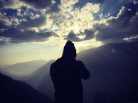 A powerful silhouette of a man wearing a leather hat, standing against a dramatic mountain backdrop.