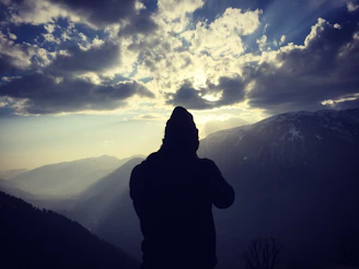 A powerful silhouette of a man wearing a leather hat, standing against a dramatic mountain backdrop.