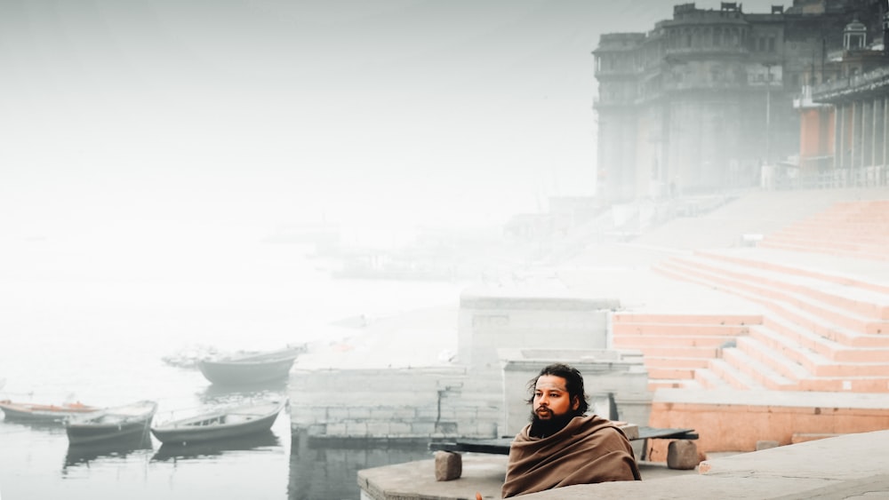 a man sitting on a ledge next to a body of water