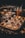 A tray filled with partially prepared pastry tarts, some topped with star-shaped dough. Ingredients include a jar of filling, likely mincemeat, spread across a dark, flour-dusted countertop. Star-shaped cookie cutters are scattered around the scene.