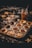 A tray filled with partially prepared pastry tarts, some topped with star-shaped dough. Ingredients include a jar of filling, likely mincemeat, spread across a dark, flour-dusted countertop. Star-shaped cookie cutters are scattered around the scene.