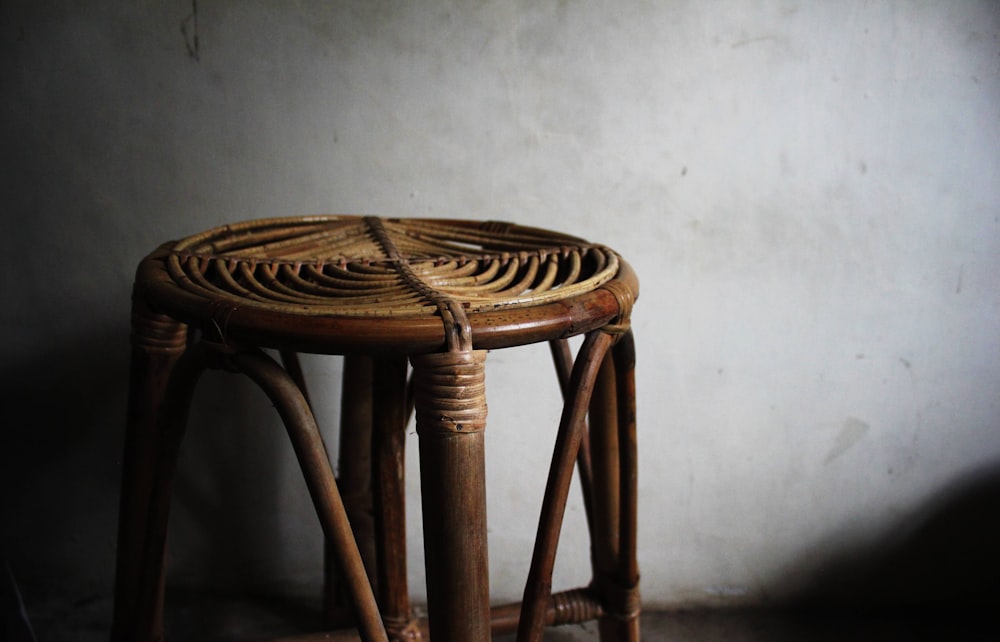 a wicker stool sits against a white wall