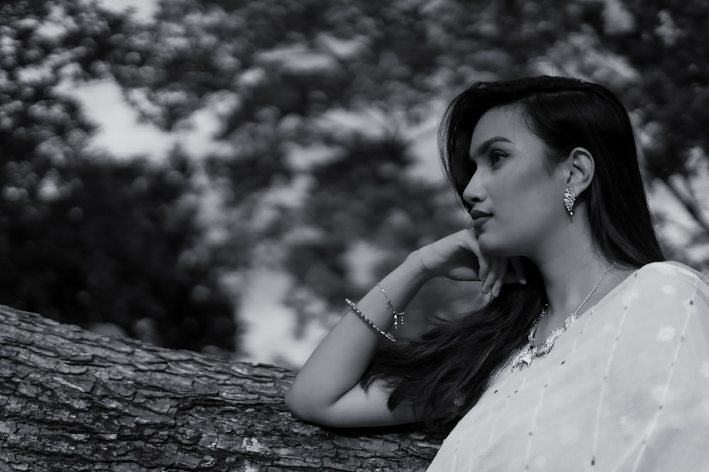 a woman leaning on a tree branch with her hand on her chin