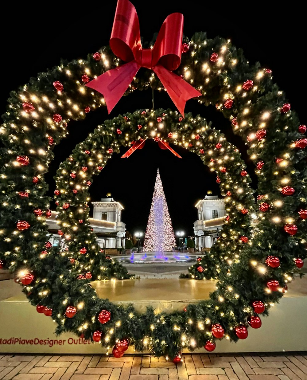a lighted christmas wreath with a christmas tree in the background