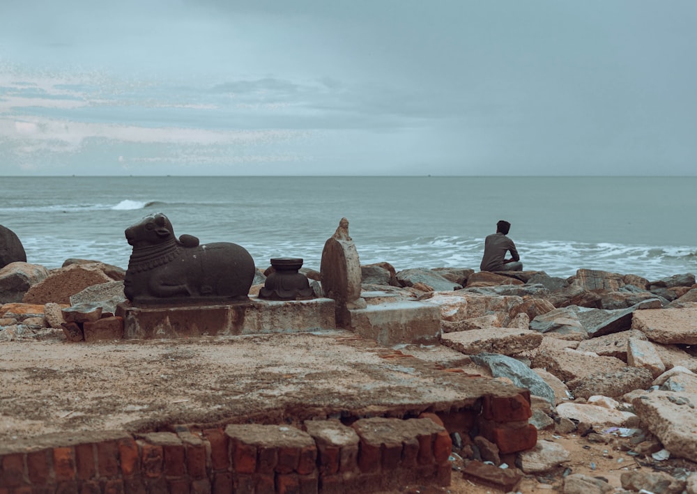 a couple of statues sitting on top of a rocky beach