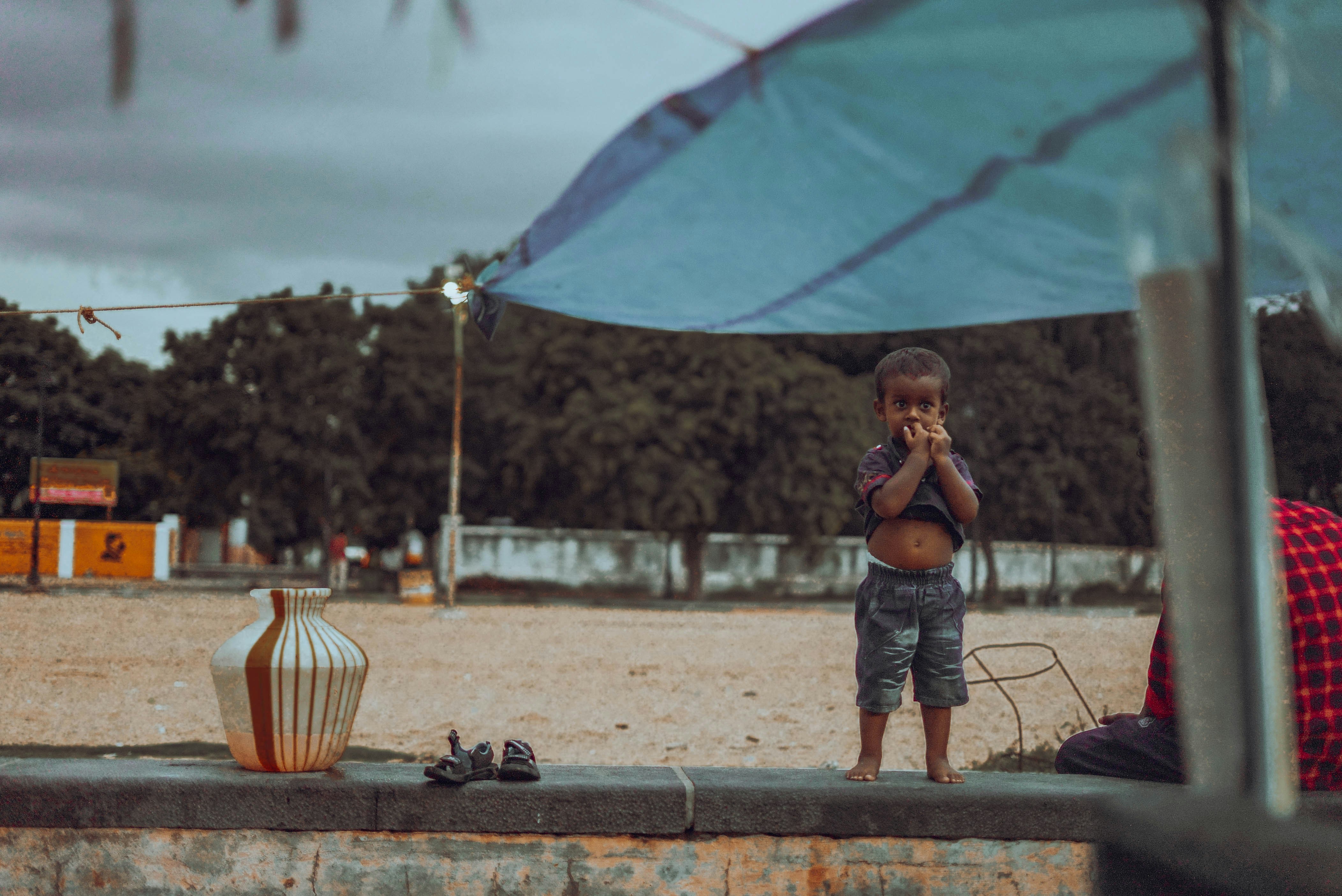 Young child stands under umbrella eating food