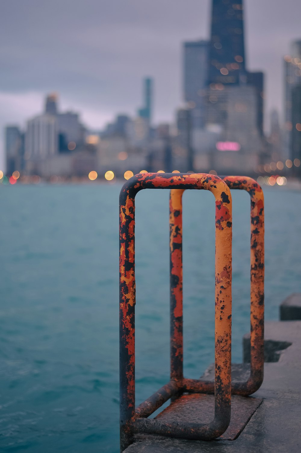 a rusted metal railing near a body of water with a city in the background