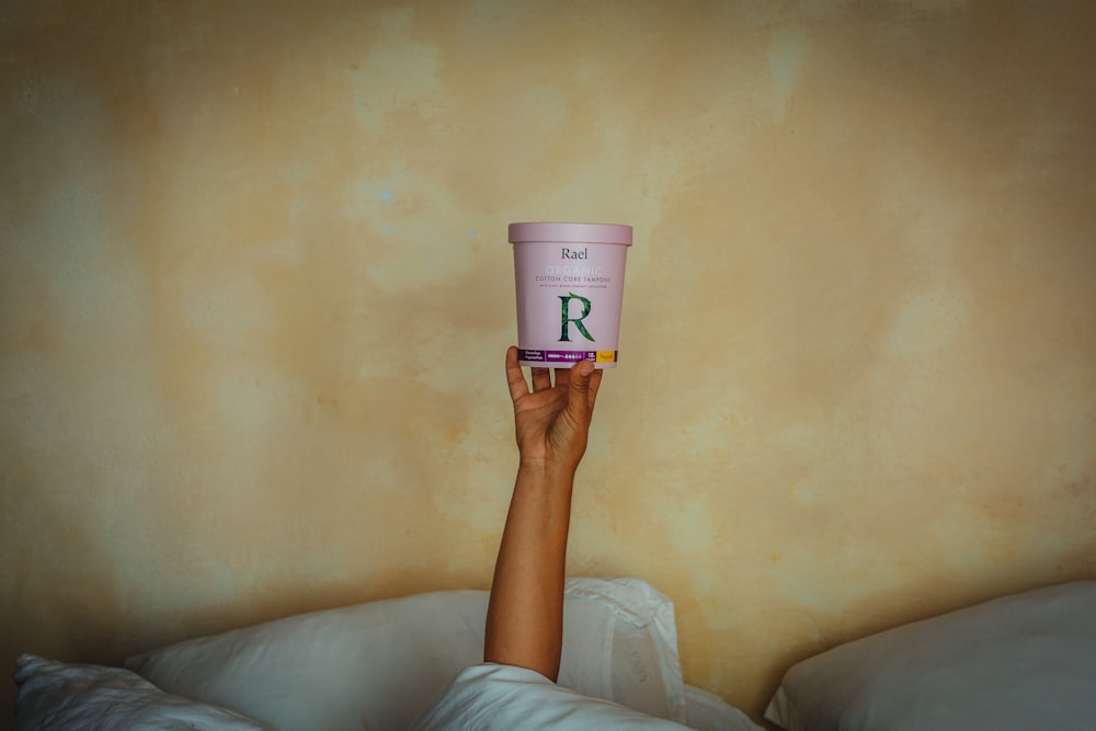 a person holding up a cup with the letter r on it