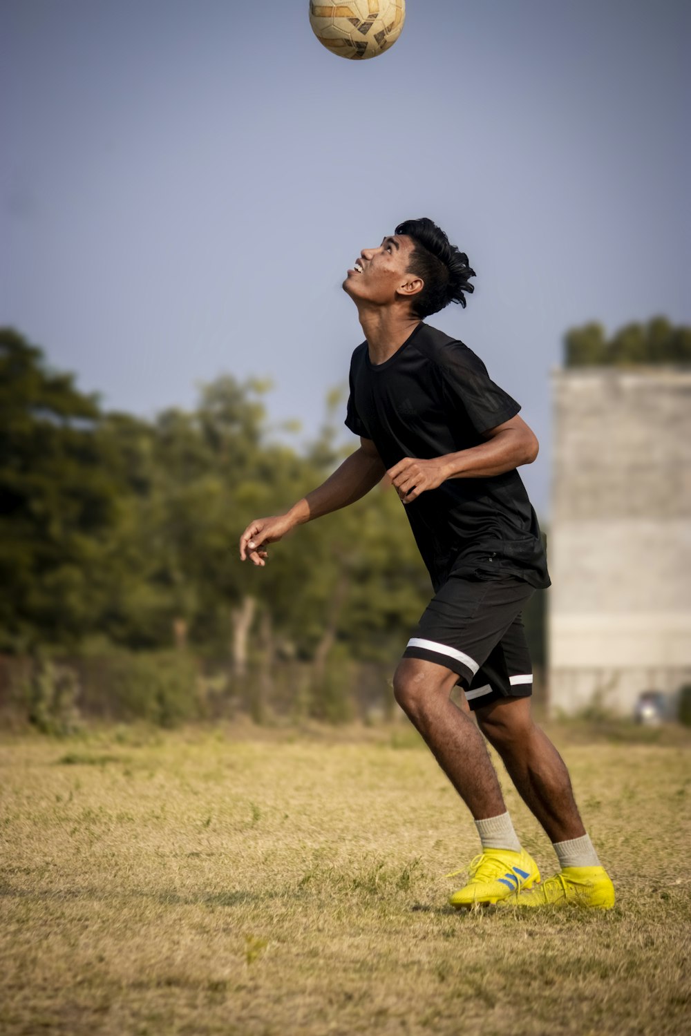 a man in black shirt and yellow shoes playing with a soccer ball