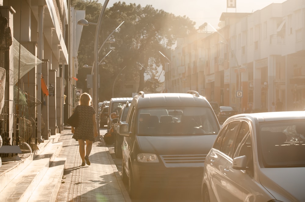 a woman walking down a street next to parked cars