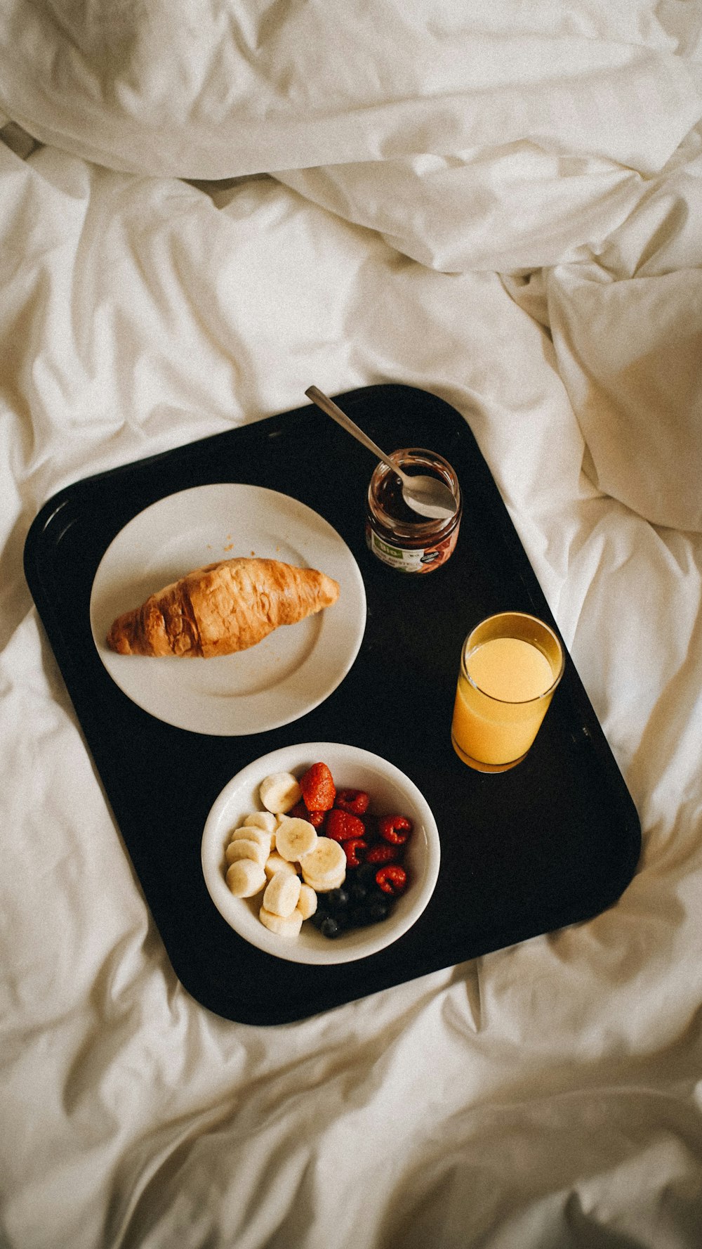 a tray of food on a bed with a glass of orange juice