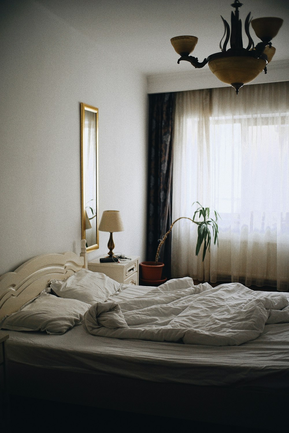an unmade bed in a bedroom next to a window