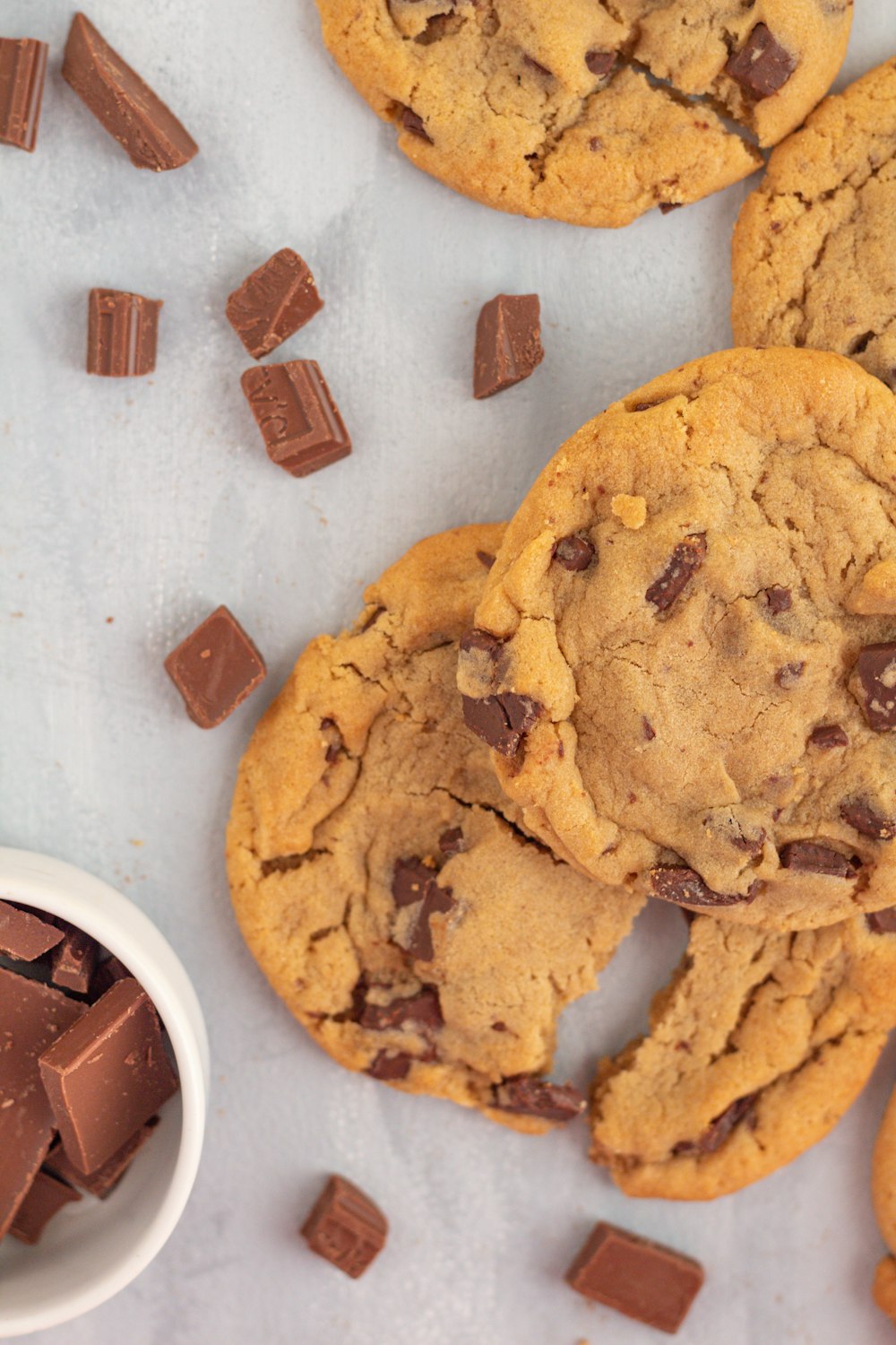 a pile of chocolate chip cookies next to a bowl of chocolate chips