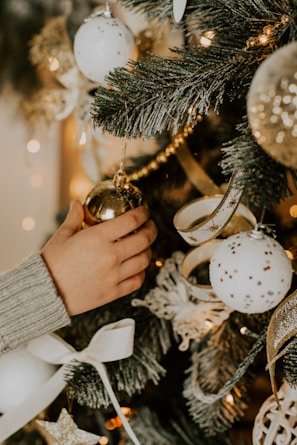A child’s hand placing a handmade ornament on a decorated tree.