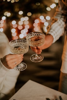 two people holding wine glasses in front of a christmas tree