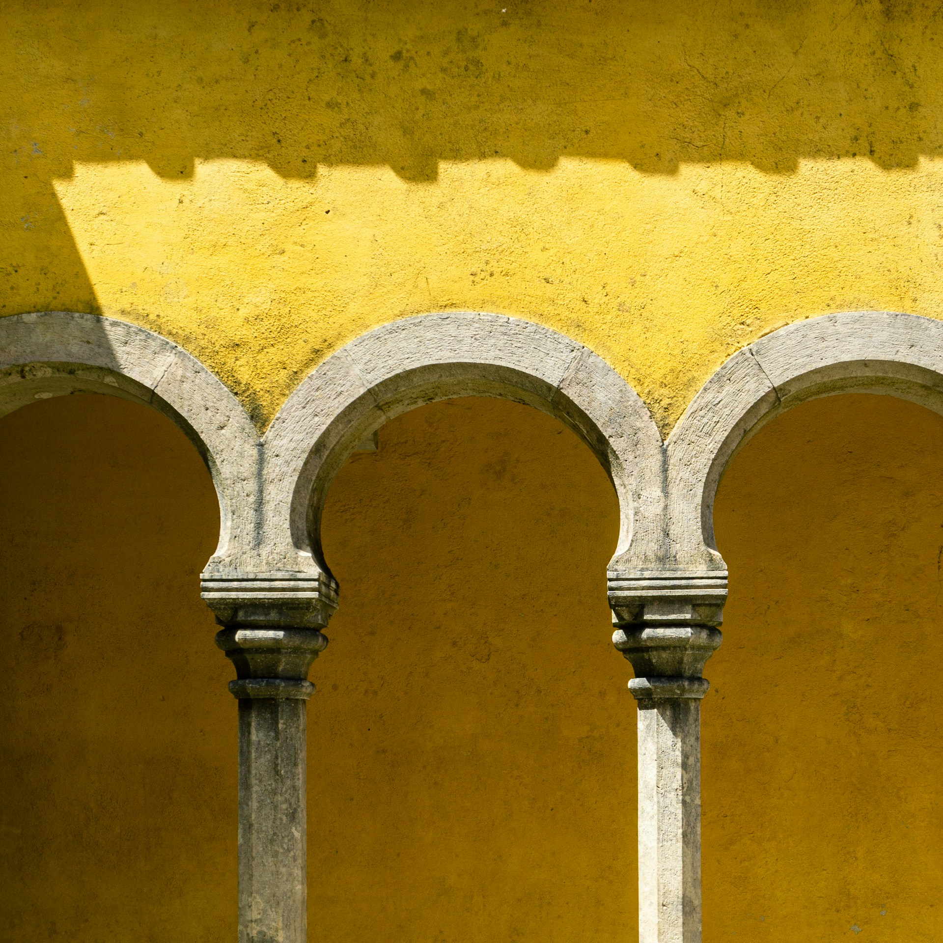 a yellow wall with arches and a clock on it