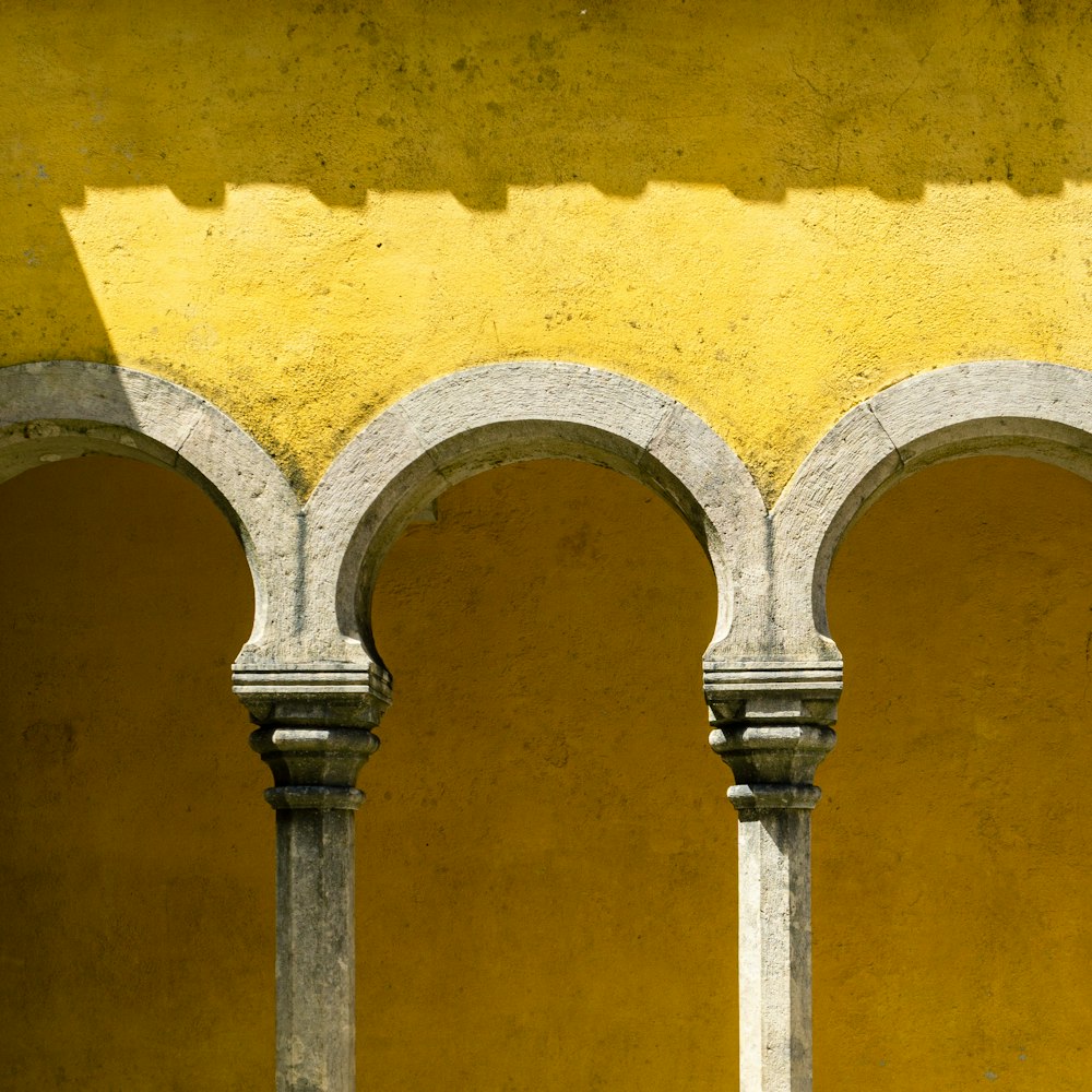 a yellow wall with arches and a clock on it