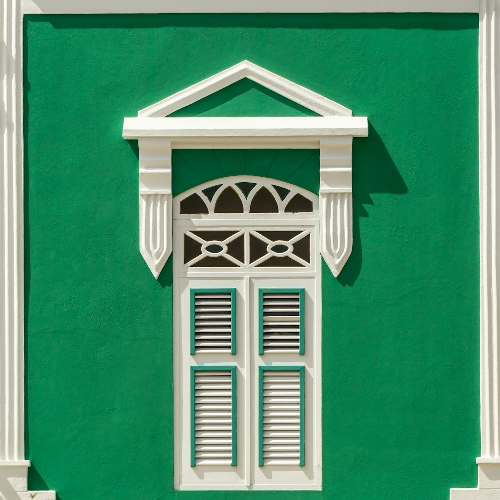 a green building with a white window and shutters
